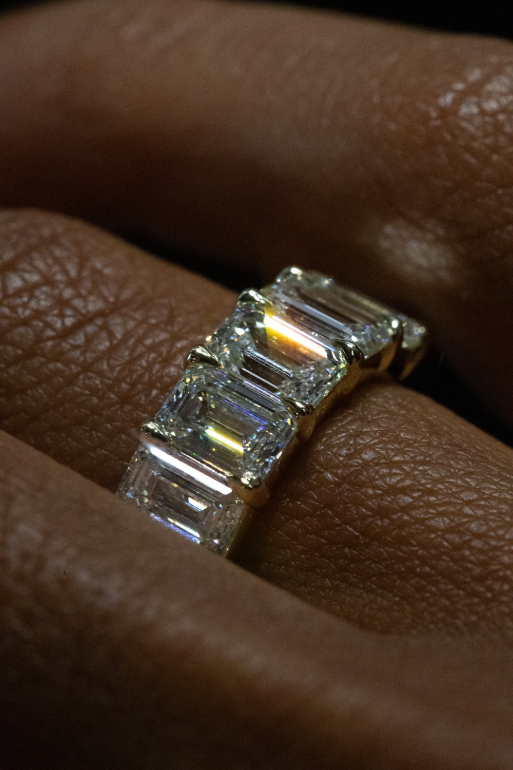 A cocktail ring set with a row of emerald-cut diamonds in yellow gold, worn on a hand